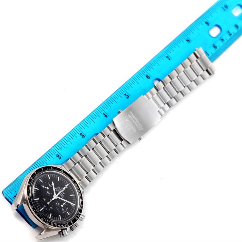 The image shows an Omega Speedmaster 3570.50.00 Men
s Stainless Steel Black Dial 3570.50.00 Men
s Stainless Steel Black Dial watch laid flat, with its face and metal bracelet next to a blue ruler.