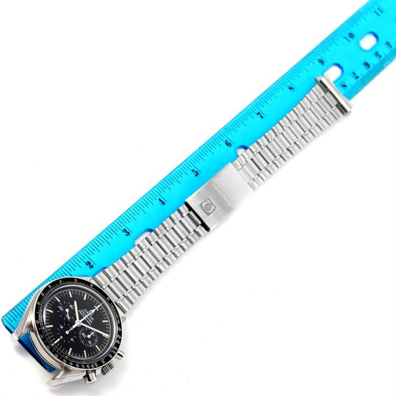 The Omega Speedmaster 3590.50.00 Men
s Stainless Steel Black Dial 3590.50.00 Men
s Stainless Steel Black Dial watch is shown at an angle displaying its dial, stainless steel bracelet, and clasp next to a blue ruler.