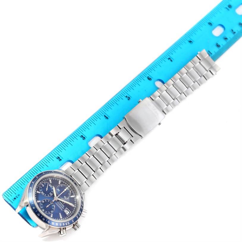 The image shows an Omega Speedmaster 3212.80.00 Men
s Stainless Steel Blue Dial 3212.80.00 Men
s Stainless Steel Blue Dial watch with its full stainless steel bracelet positioned next to a blue ruler.