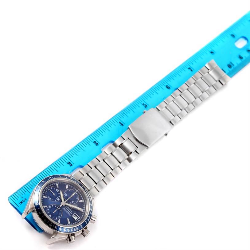 The image shows an Omega Speedmaster 3212.80.00 Men
s Stainless Steel Blue Dial 3212.80.00 Men
s Stainless Steel Blue Dial watch laid next to a blue ruler, showcasing its dial and metal bracelet.