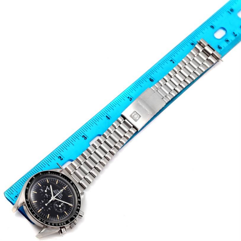 The Omega Speedmaster 3590.50.00 Men
s Stainless Steel Black Dial 3590.50.00 Men
s Stainless Steel Black Dial watch is shown from an upper angle, displaying its dial and metal bracelet along with a blue measuring ruler.