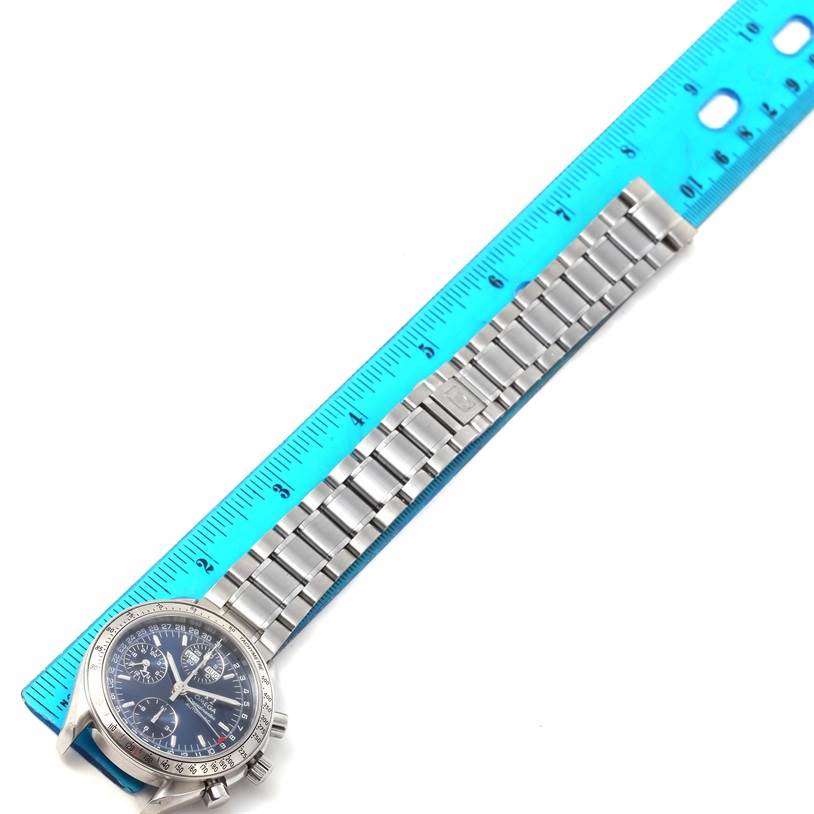 This image shows an Omega Speedmaster 3523.80.00 Men
s Stainless Steel Blue Dial 3523.80.00 Men
s Stainless Steel Blue Dial watch laid flat with its metal bracelet aligned next to a blue ruler.