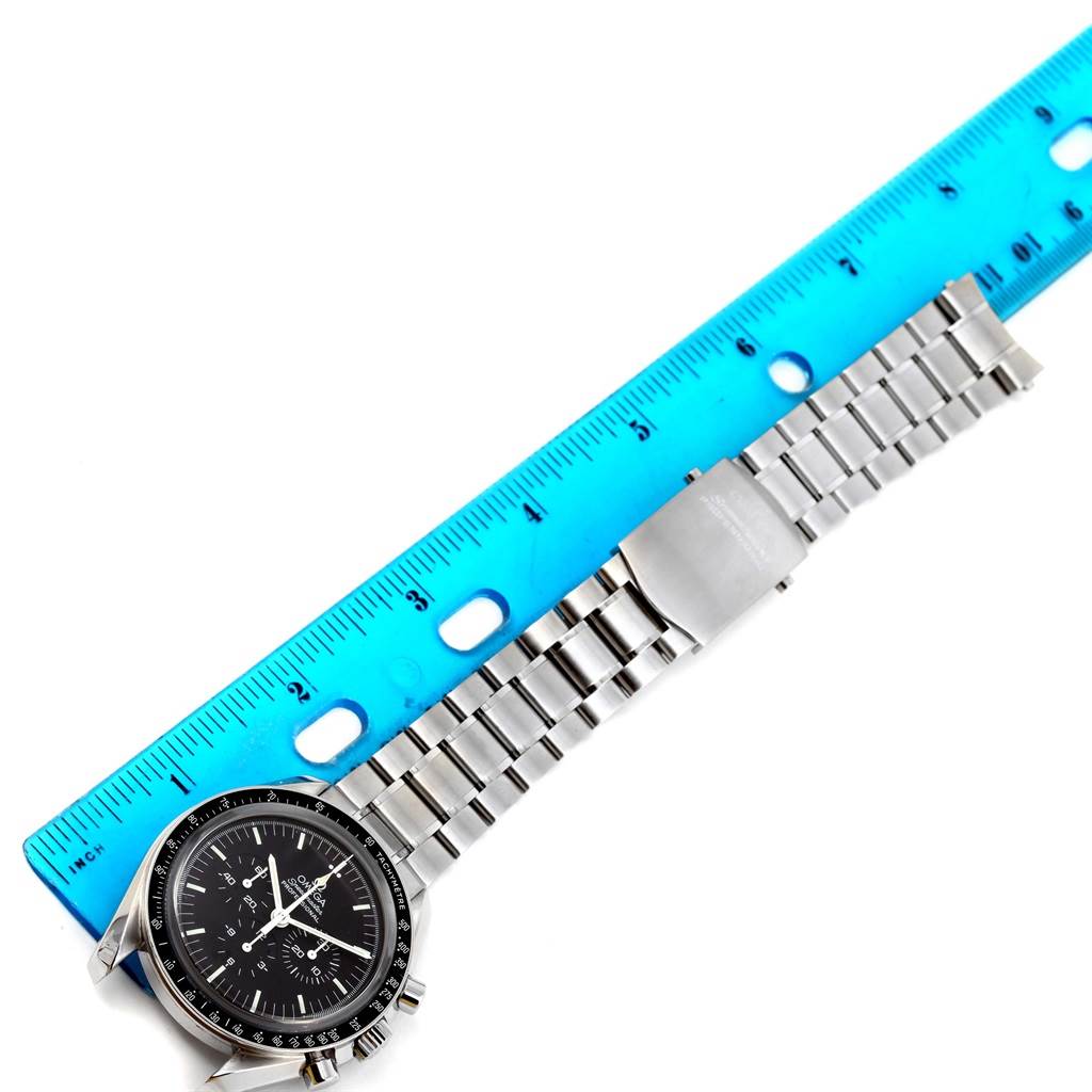 The Omega Speedmaster 3573.50.00 Men
s Stainless Steel Black Dial 3573.50.00 Men
s Stainless Steel Black Dial watch is shown diagonally from the front with its face and metal bracelet alongside a blue ruler.