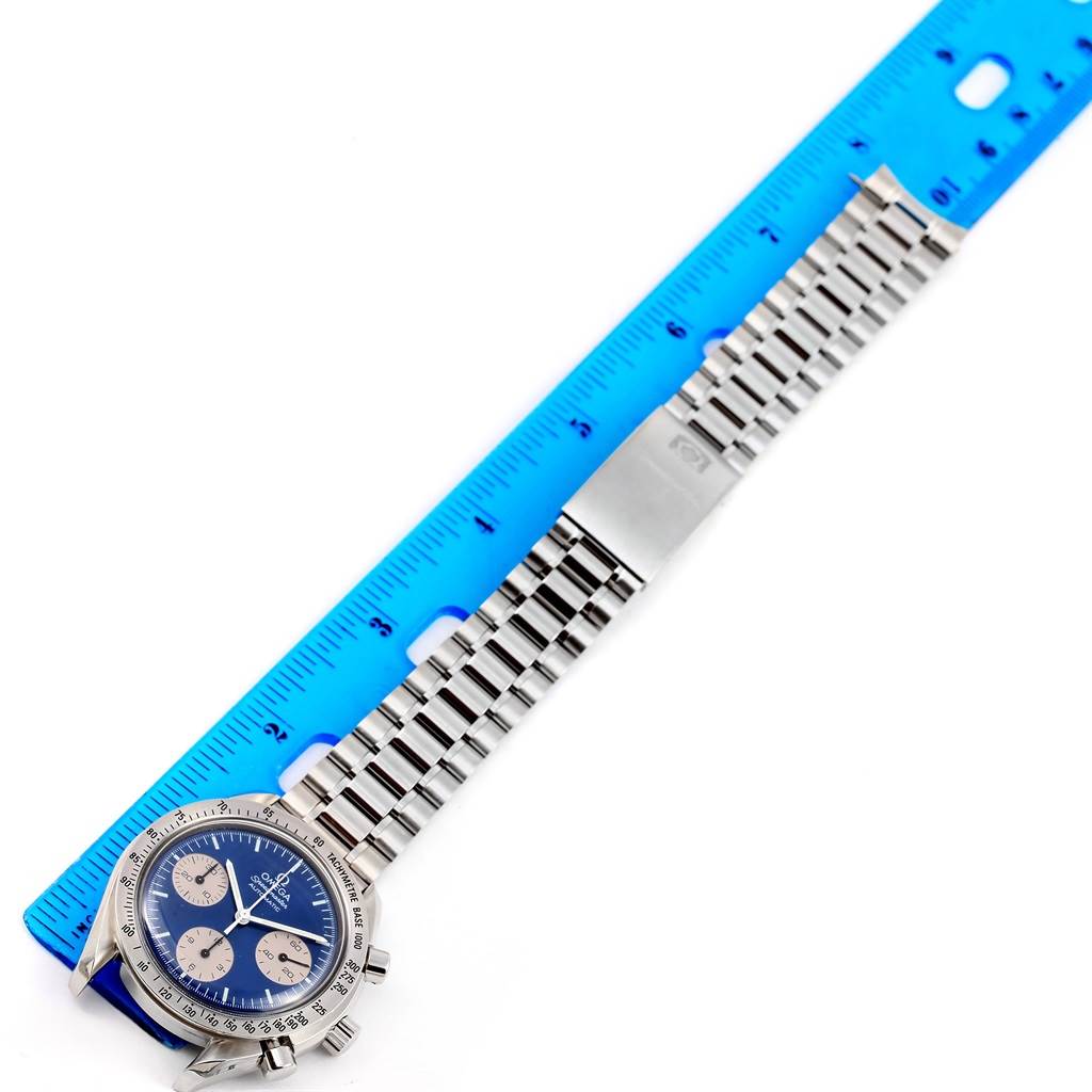 The image shows an Omega Speedmaster 3510.82.00 Men
s Stainless Steel Blue Dial 3510.82.00 Men
s Stainless Steel Blue Dial watch with a stainless steel bracelet laid next to a blue ruler, photographed from above.