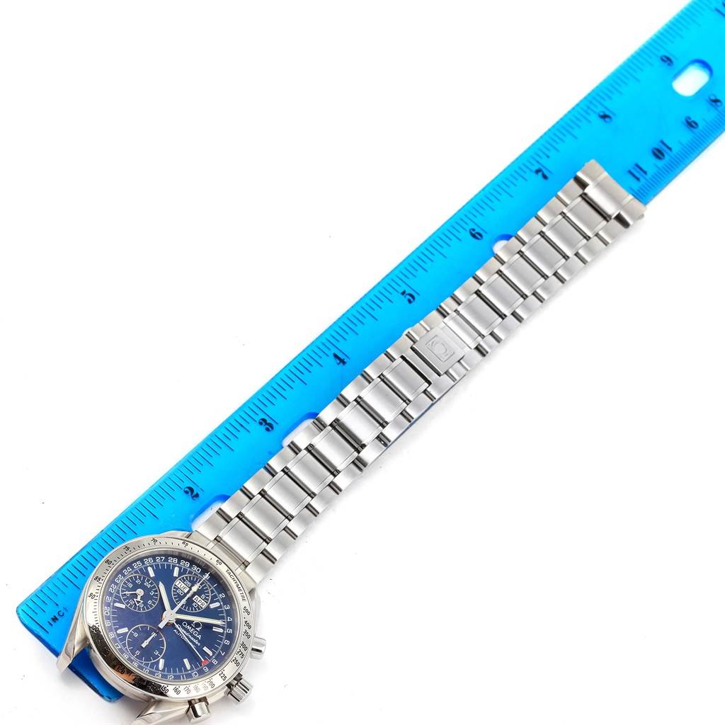 The image shows an Omega Speedmaster 3523.80.00 Men
s Stainless Steel Blue Dial 3523.80.00 Men
s Stainless Steel Blue Dial watch with its metal bracelet aligned against a blue ruler.