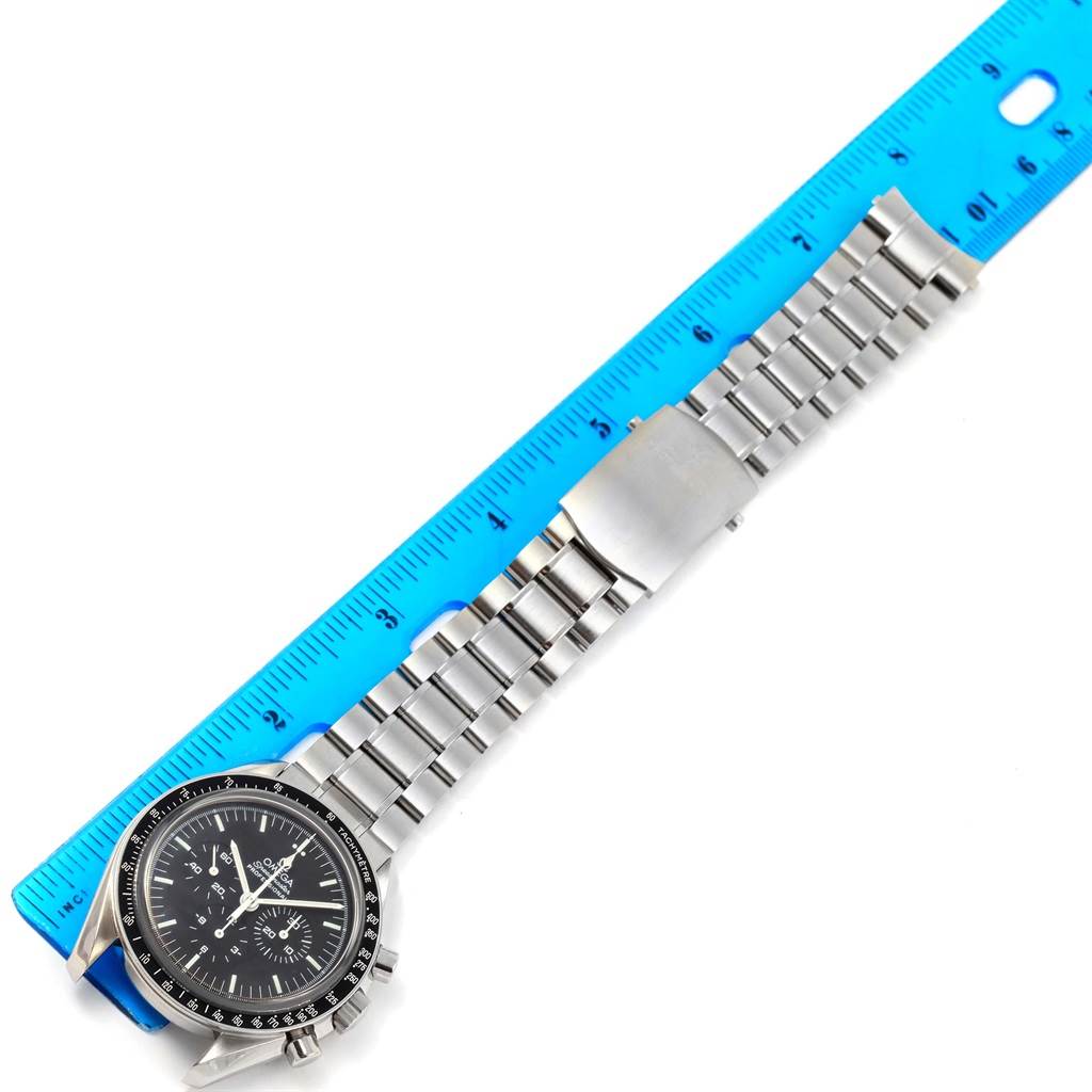 The image shows an Omega Speedmaster 3573.50.00 Men
s Stainless Steel Black Dial 3573.50.00 Men
s Stainless Steel Black Dial watch and its full stainless steel bracelet aligned with a blue ruler for measurement.