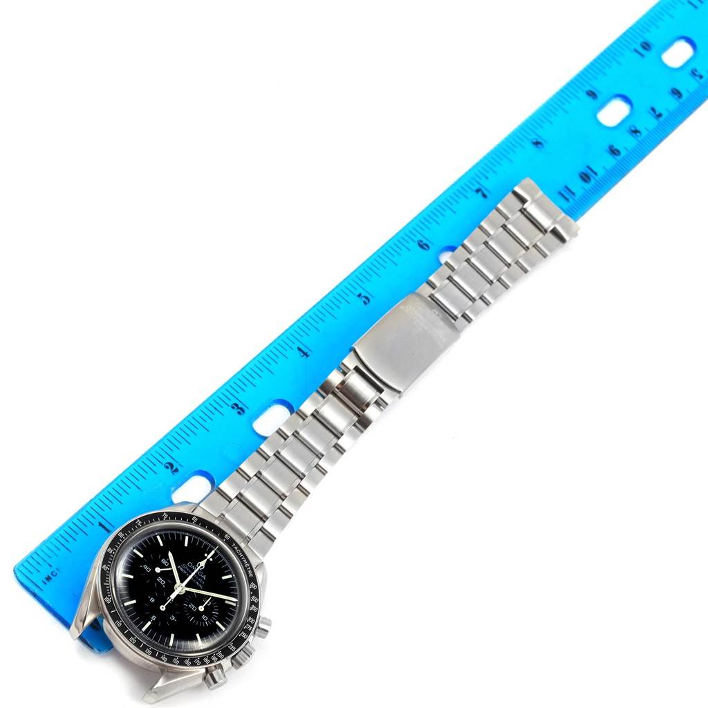 The image shows an Omega Speedmaster 3570.50.00 Men
s Stainless Steel Black Dial 3570.50.00 Men
s Stainless Steel Black Dial watch laid flat with its entire bracelet and part of the bezel and face visible, measured against a blue ruler.