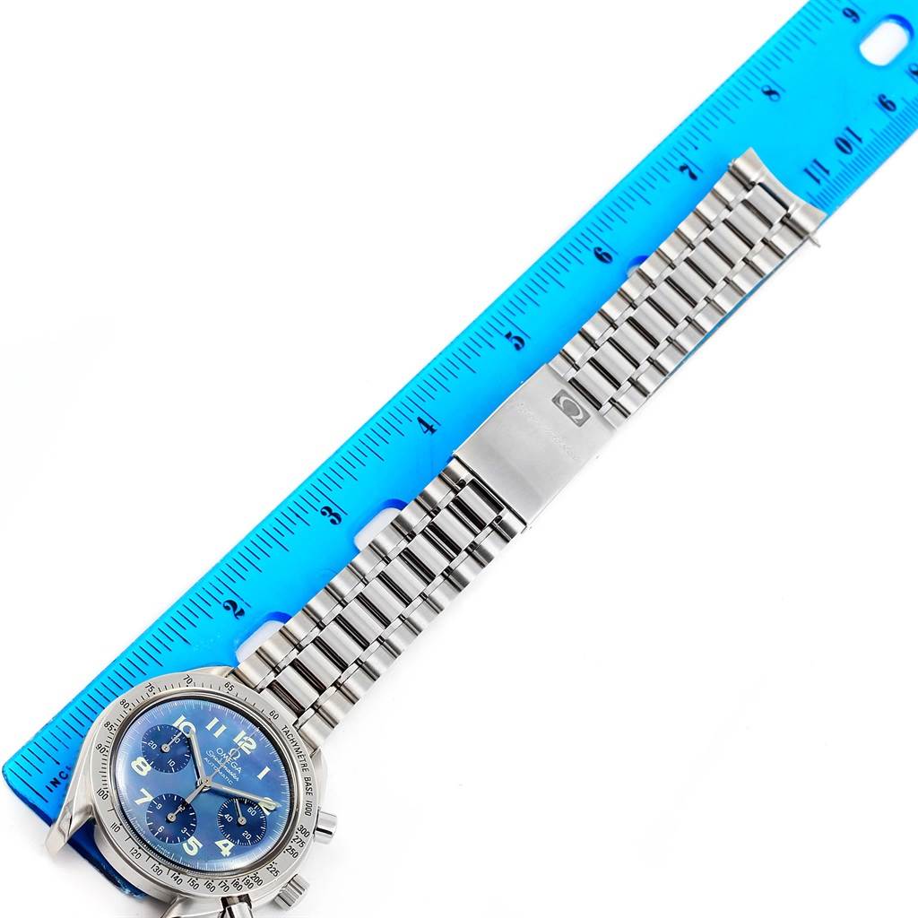 An Omega Speedmaster 3502.73.00 Men's Stainless Steel Mother of Pearl Dial 3502.73.00 Men's Stainless Steel Mother of Pearl Dial watch is shown from an overhead angle, displaying the face and full metal strap alongside a blue ruler.