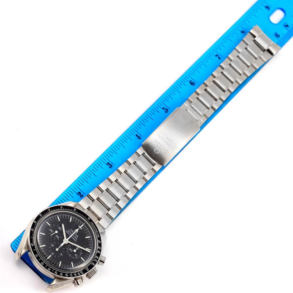 The image shows an Omega Speedmaster 3570.50.00 Men
s Stainless Steel Black Dial 3570.50.00 Men
s Stainless Steel Black Dial watch from the top angle, displaying its face, bezel, and full metal bracelet laid on a blue ruler.