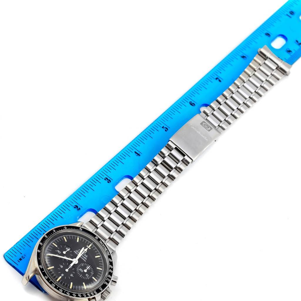 The image shows an Omega Speedmaster Men
s Stainless Steel Black Dial Men
s Stainless Steel Black Dial watch placed next to a blue ruler, displaying the watch face and metal bracelet.