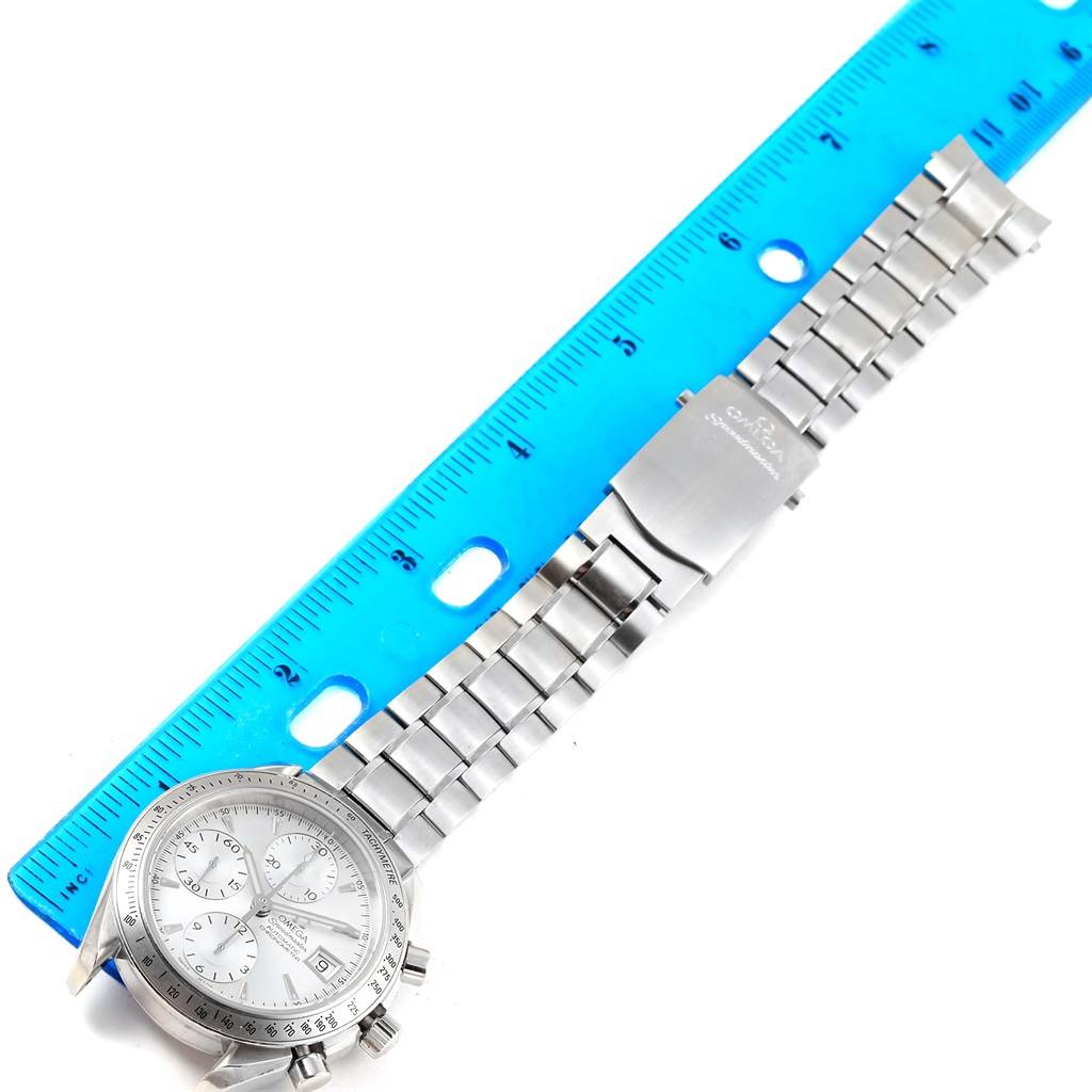 The image shows an Omega Speedmaster 3211.30.00 Men
s Stainless Steel Silver Dial 3211.30.00 Men
s Stainless Steel Silver Dial watch laid flat, with a metal bracelet and clasp visible, next to a blue ruler for scale.