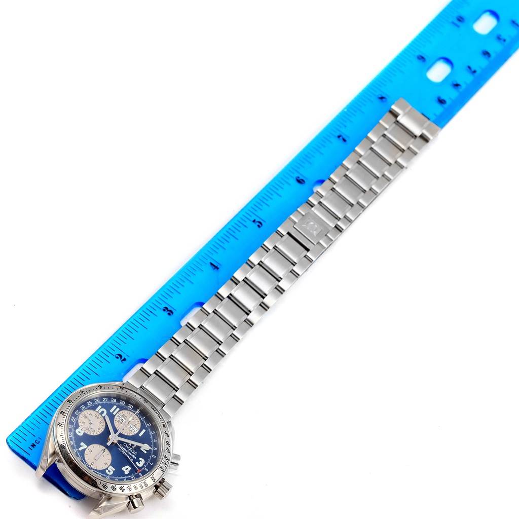 The image shows an Omega Speedmaster 3523.81.00 Men's Stainless Steel Blue Dial 3523.81.00 Men's Stainless Steel Blue Dial watch and stainless steel bracelet laid beside a blue ruler for scale.