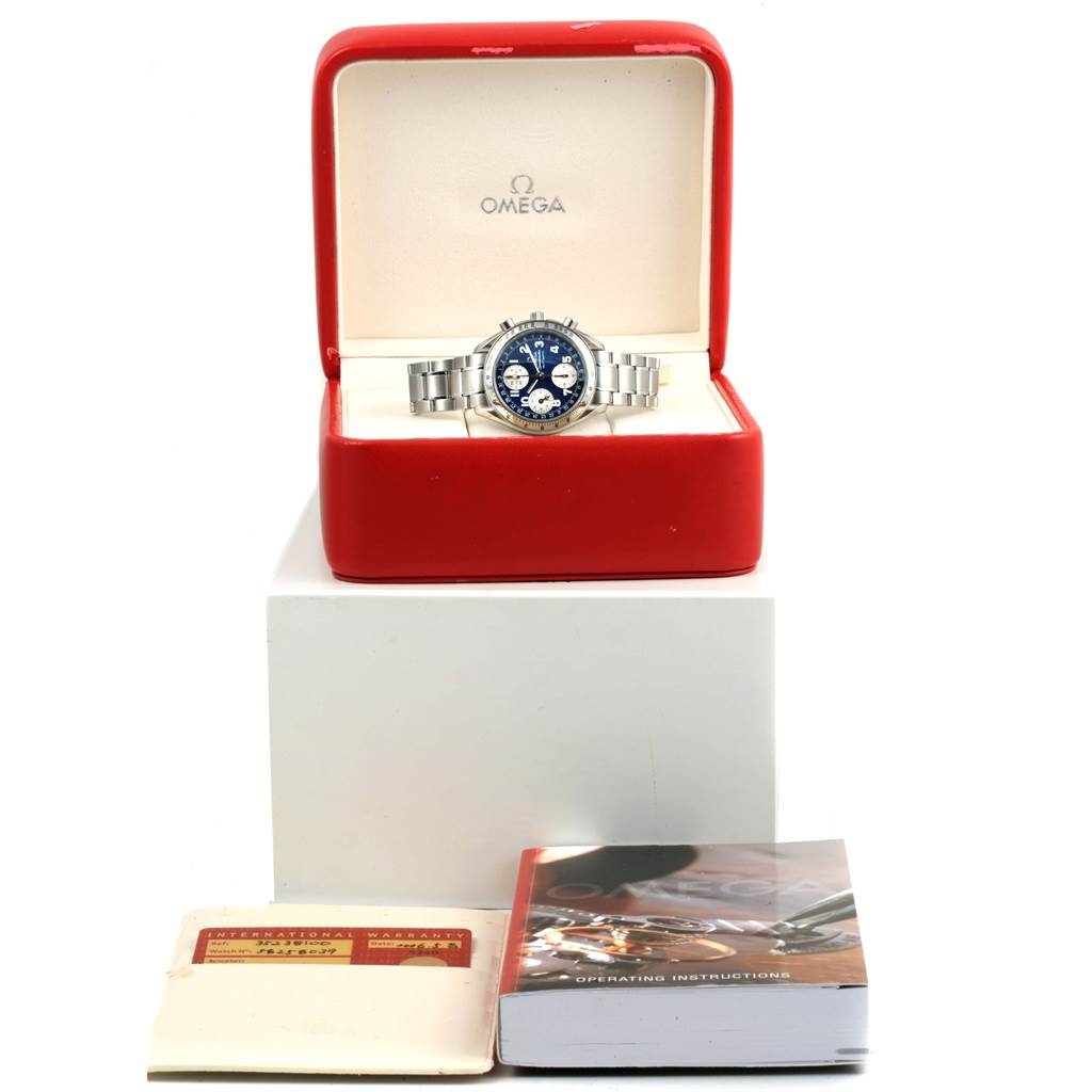 The image shows an Omega Speedmaster 3523.81.00 Men's Stainless Steel Blue Dial 3523.81.00 Men's Stainless Steel Blue Dial watch in a red and white display case, along with an international warranty card and an operating manual.