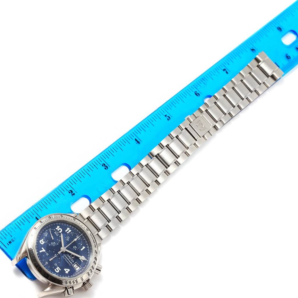 The image shows an Omega Speedmaster 3513.82.00 Men
s Stainless Steel Blue Dial 3513.82.00 Men
s Stainless Steel Blue Dial watch and its metal bracelet laid out next to a ruler for measurement.