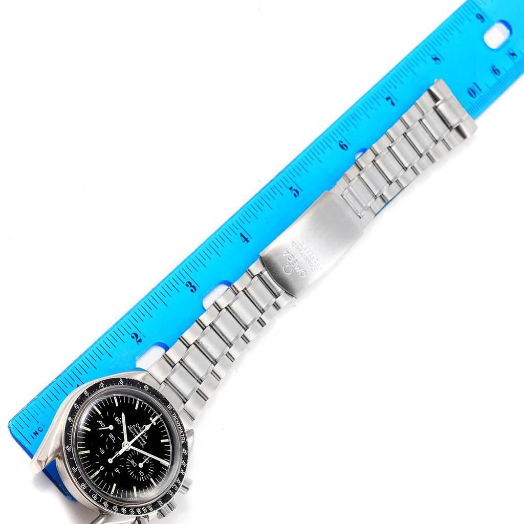 The image shows an Omega Speedmaster Men
s Stainless Steel Black Dial Men
s Stainless Steel Black Dial watch laying flat against a blue ruler, showcasing its face, bezel, and stainless steel bracelet.