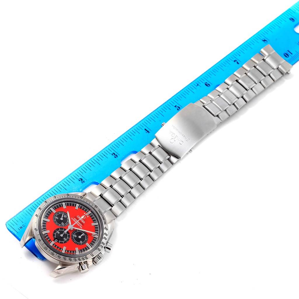 The image shows an Omega Speedmaster 3506.61.00 Men's Stainless Steel Red Dial 3506.61.00 Men's Stainless Steel Red Dial watch laid flat against a blue ruler, displaying the face, case, and metal bracelet.