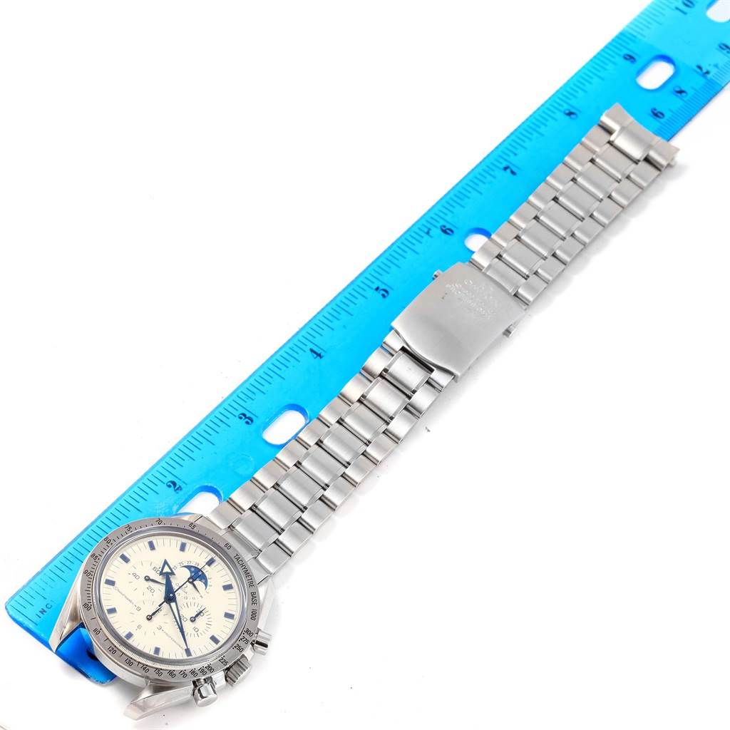 The Omega Speedmaster 3575.20.00 Men's Stainless Steel White Dial 3575.20.00 Men's Stainless Steel White Dial watch is shown at an overhead angle, highlighting its face and metal bracelet alongside a blue ruler.