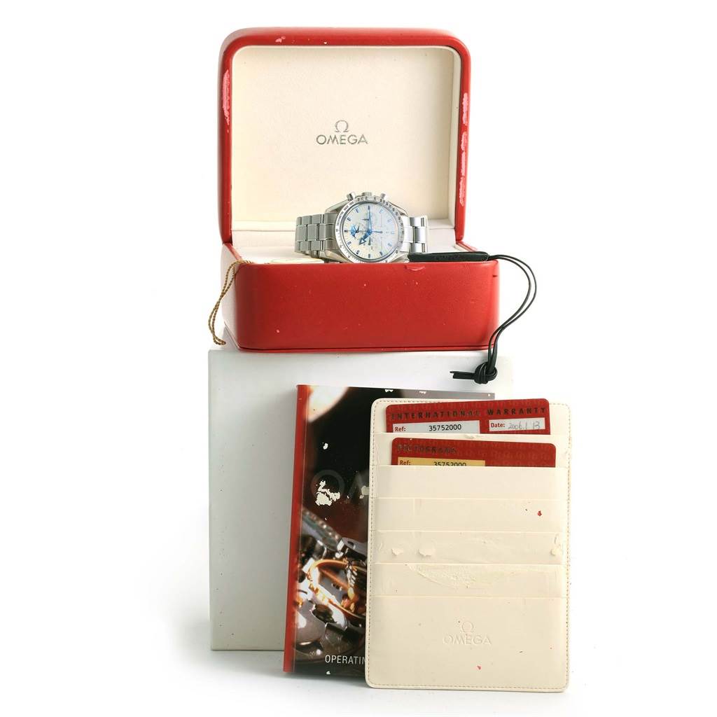 The Omega Speedmaster 3575.20.00 Men's Stainless Steel White Dial 3575.20.00 Men's Stainless Steel White Dial watch is shown from the front, displayed in its open box, along with the warranty card and an operating manual.