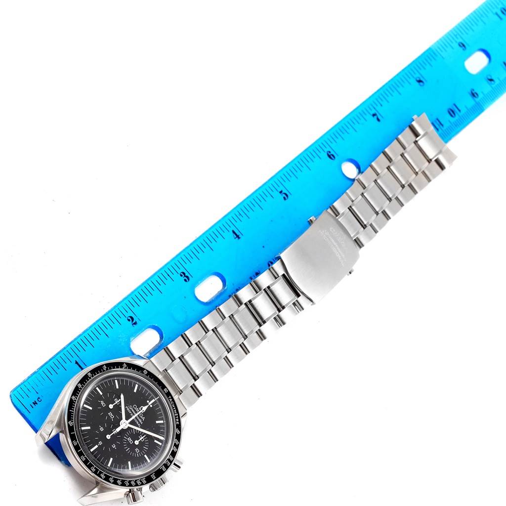 The image shows an Omega Speedmaster 3570.50.00 Men's Stainless Steel Black Dial 3570.50.00 Men's Stainless Steel Black Dial watch laid flat with the bracelet and clasp extended against a blue ruler for measurement.