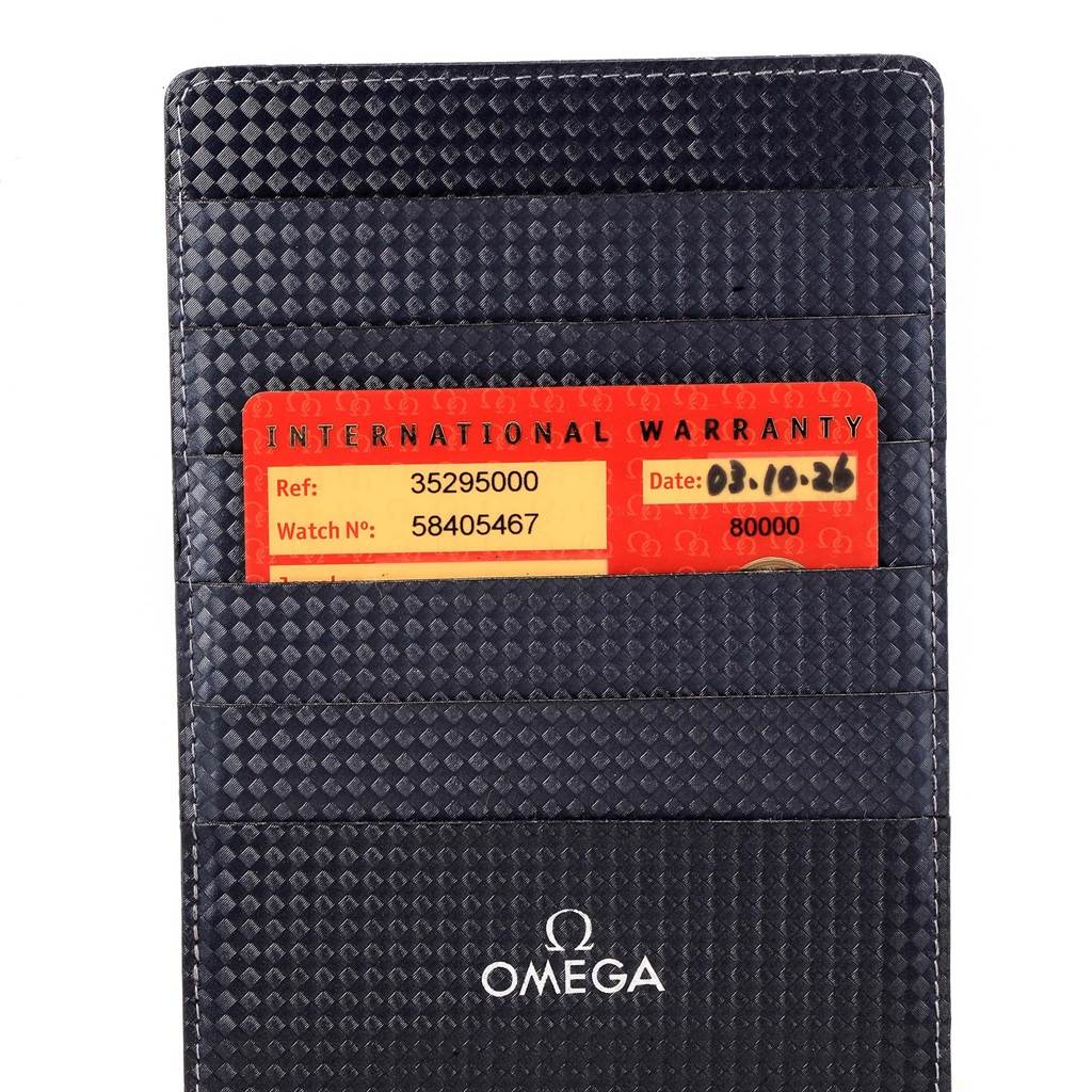 The image shows a close-up of an Omega Speedmaster 3529.50.00 Men's Stainless Steel Black Dial 3529.50.00 Men's Stainless Steel Black Dial's international warranty card and cardholder.