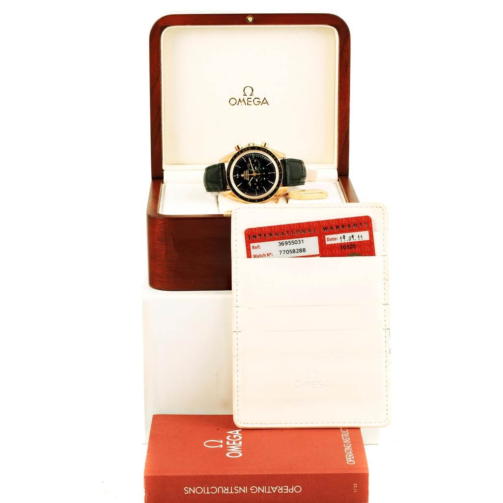 The Omega Speedmaster 3695.50.31 Men's Yellow Gold Black Dial 3695.50.31 Men's Yellow Gold Black Dial watch is displayed front-facing in a wooden box, accompanied by warranty cards and an operating instructions manual.