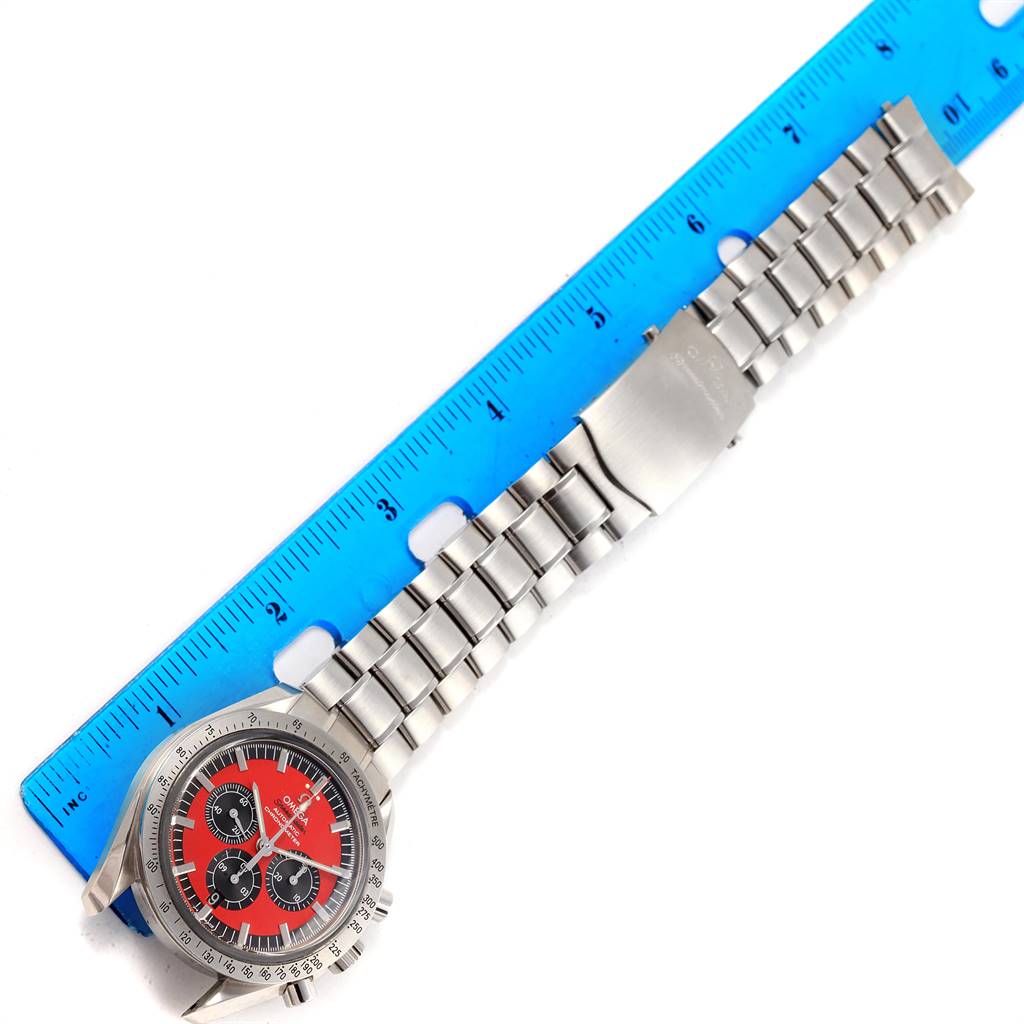 The image shows an Omega Speedmaster 3506.61.00 Men
s Stainless Steel Red Dial 3506.61.00 Men
s Stainless Steel Red Dial watch with a stainless steel bracelet next to a blue ruler, viewed from above.
