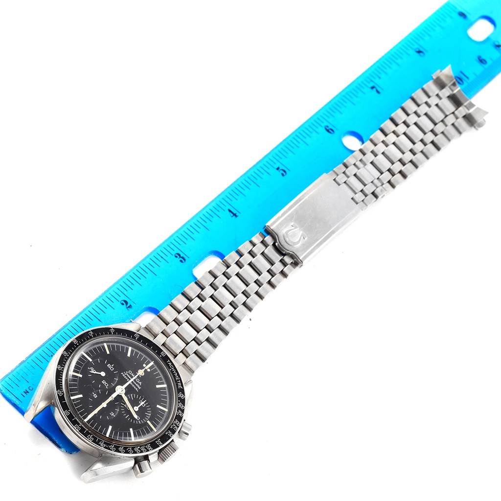 The Omega Speedmaster Men
s Stainless Steel Black Dial Men
s Stainless Steel Black Dial watch is shown flat with a silver bracelet next to a blue ruler.