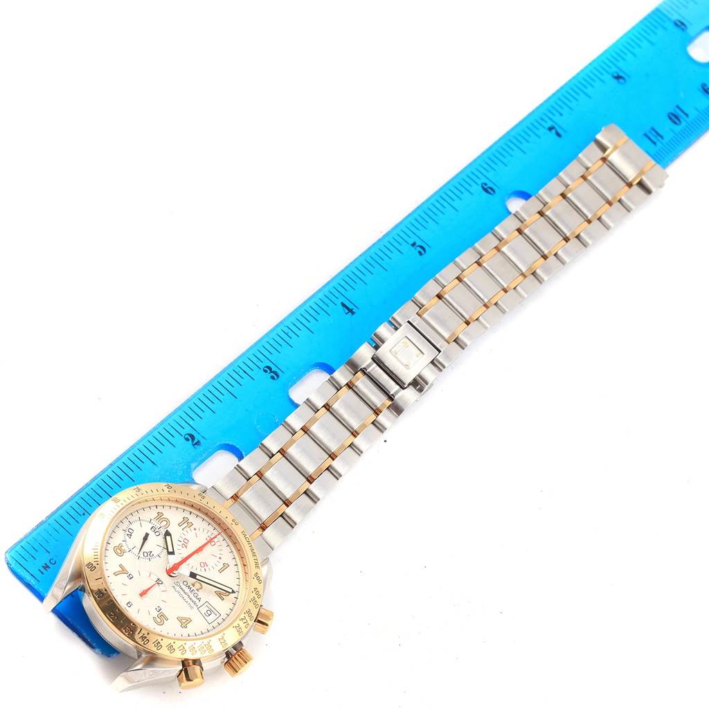 The Omega Speedmaster 3313.33.00 Men's Steel and Gold (two tone) White Dial 3313.33.00 Men's Steel and Gold (two tone) White Dial watch is shown from an above angle, displaying the face, bezel, bracelet, and top chronograph pushers alongside a ruler.