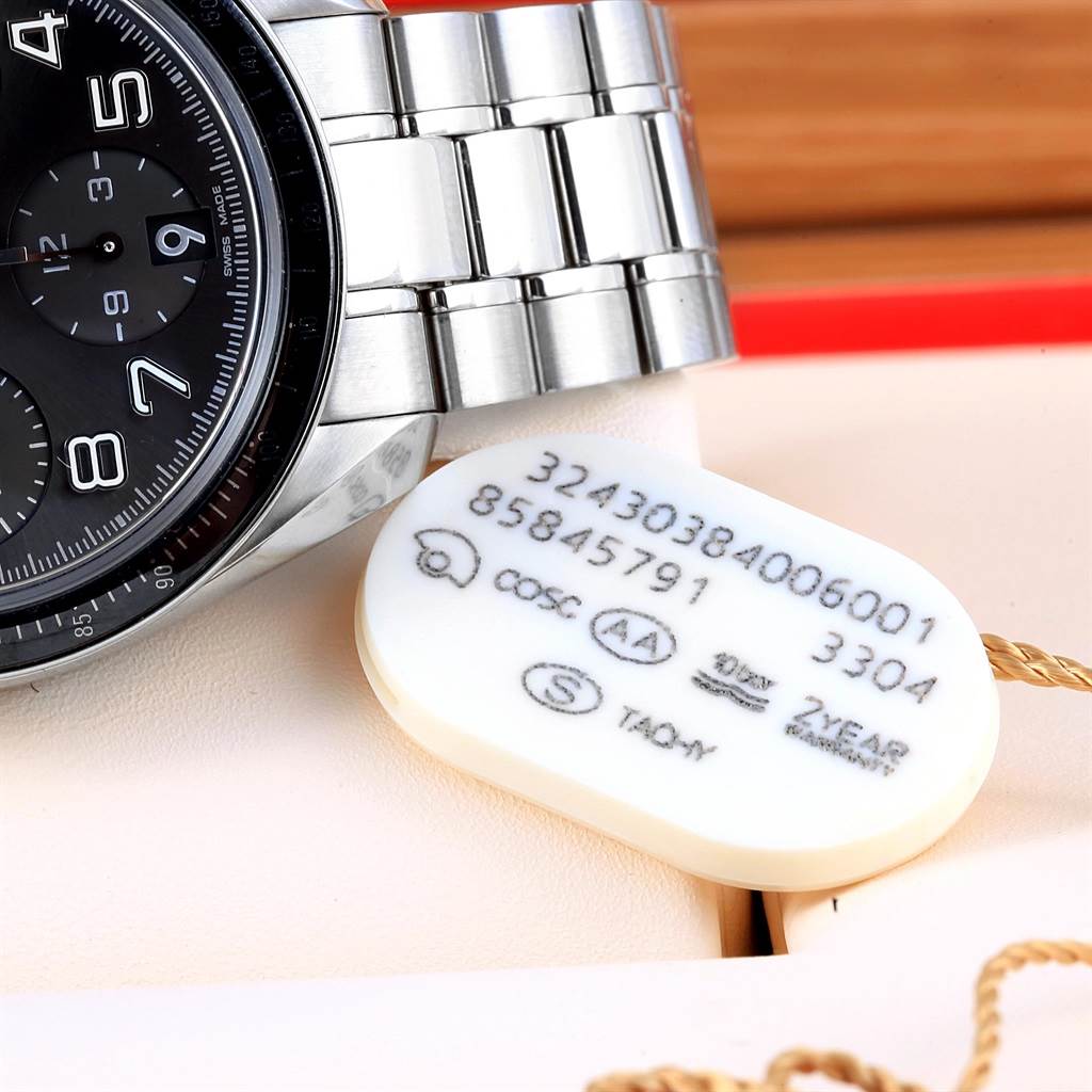 The image shows a partial view of an Omega Speedmaster 324.30.38.40.06.001 Men
s Stainless Steel Grey Dial 324.30.38.40.06.001 Men
s Stainless Steel Grey Dial watch face and metal band, alongside its tag with reference numbers.