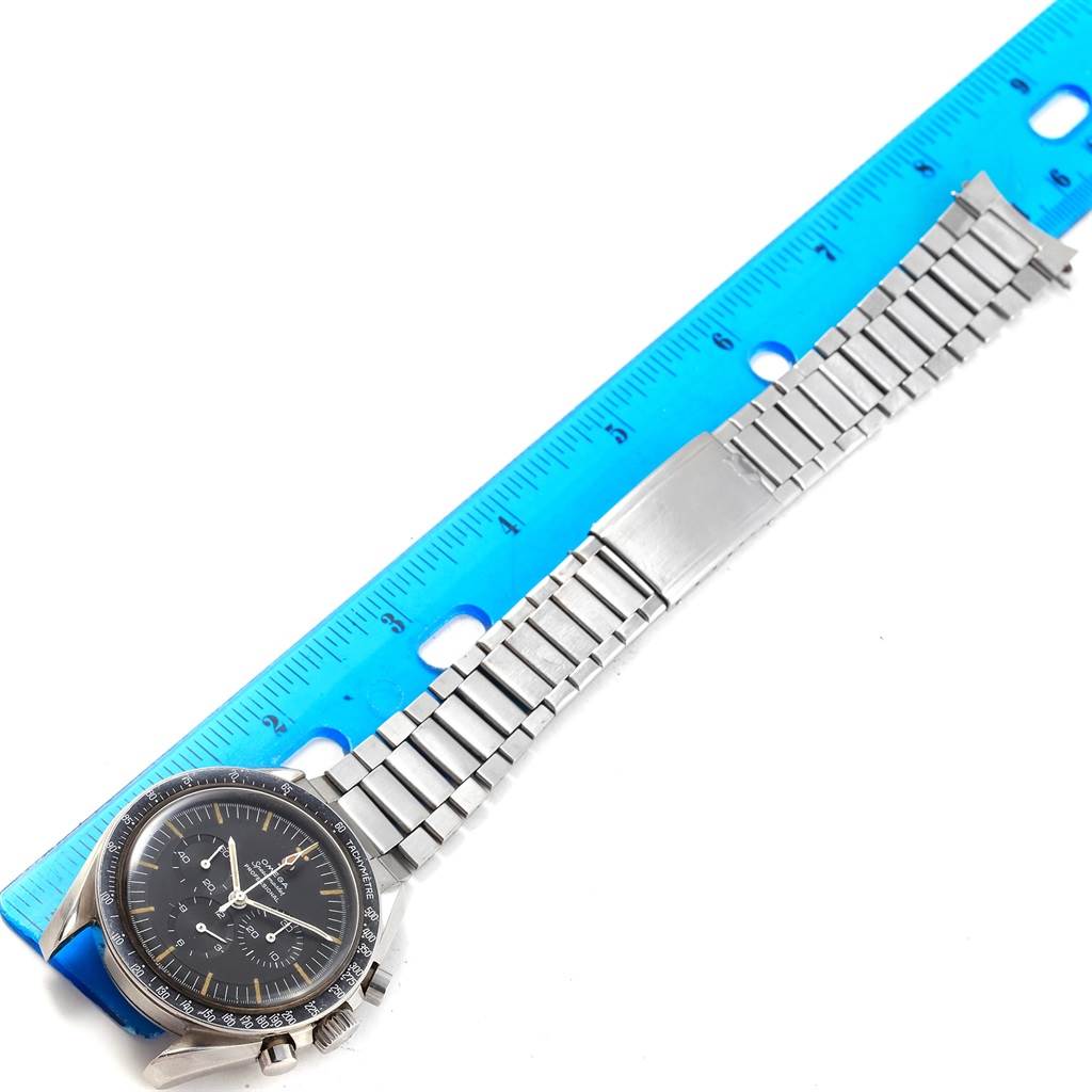 This image shows an Omega Speedmaster 105.012-64 Men's Stainless Steel Black Dial 105.012-64 Men's Stainless Steel Black Dial watch from a top-down angle, highlighting the dial, bezel, and metal bracelet with a blue ruler for scale.