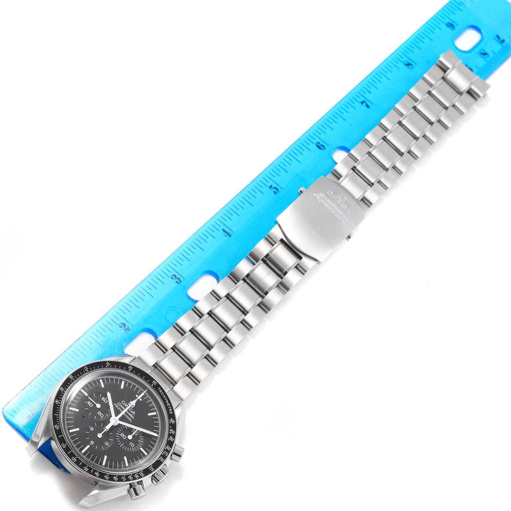 The image shows an overhead view of an Omega Speedmaster 311.30.42.30.01.005 Men
s Stainless Steel Black Dial 311.30.42.30.01.005 Men
s Stainless Steel Black Dial watch, with its bracelet laid on a blue ruler.