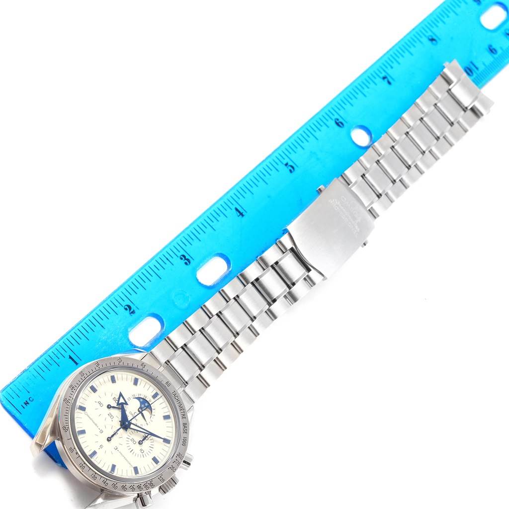 The Omega Speedmaster 3575.20.00 Men
s Stainless Steel White Dial 3575.20.00 Men
s Stainless Steel White Dial watch is shown laid flat with its face, bezel, and metal bracelet next to a blue ruler.