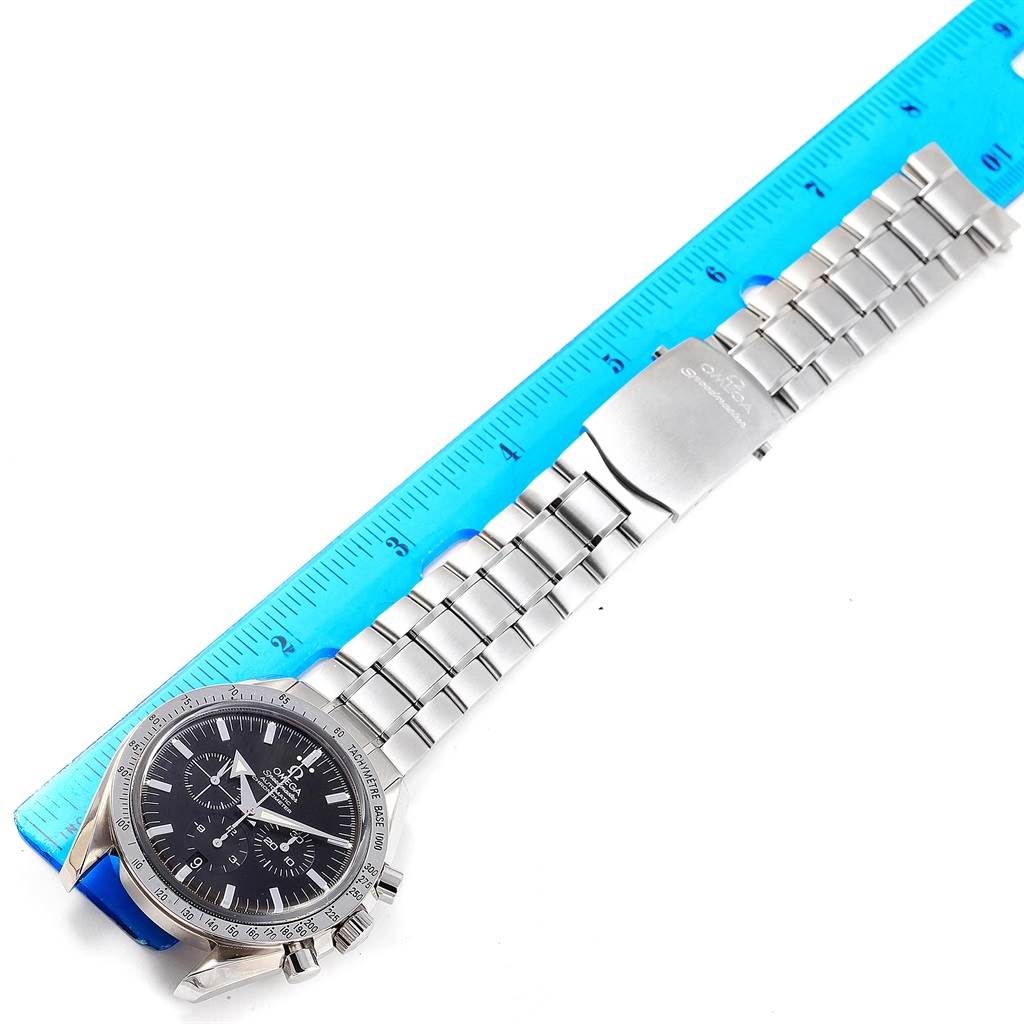 The image shows an Omega Speedmaster 3551.50.00 Men
s Stainless Steel Black Dial 3551.50.00 Men
s Stainless Steel Black Dial watch laid flat with a metal bracelet, aligned next to a blue ruler.