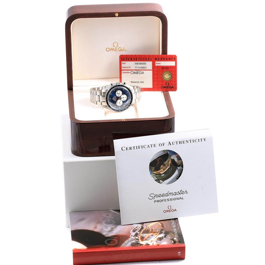 The image shows an Omega Speedmaster 3565.80.00 Men's Stainless Steel Blue Dial 3565.80.00 Men's Stainless Steel Blue Dial watch in its open case, with warranty card, certificate of authenticity, and manual.