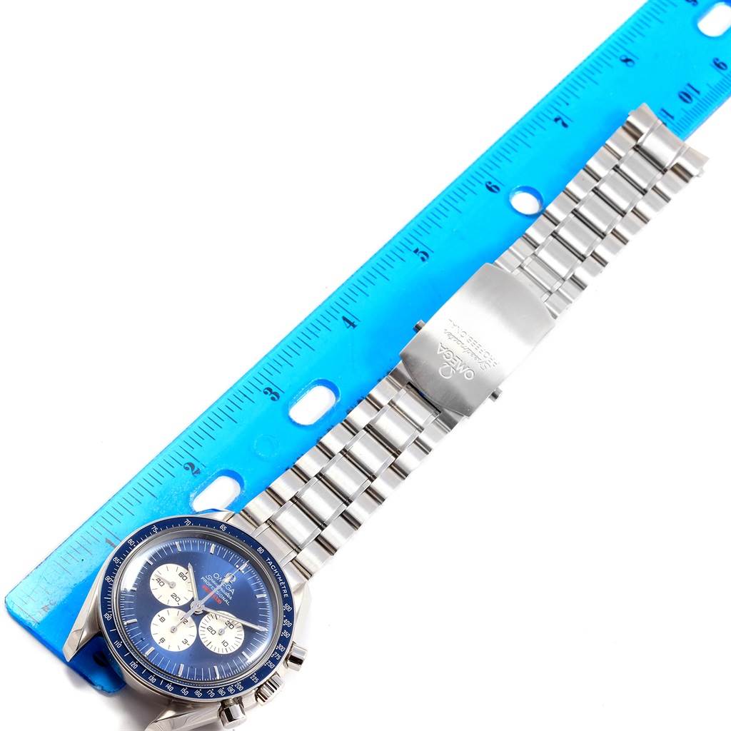 This image shows an Omega Speedmaster 3565.80.00 Men's Stainless Steel Blue Dial 3565.80.00 Men's Stainless Steel Blue Dial watch laid flat, with its clasp and bracelet extended alongside a blue ruler for scale.