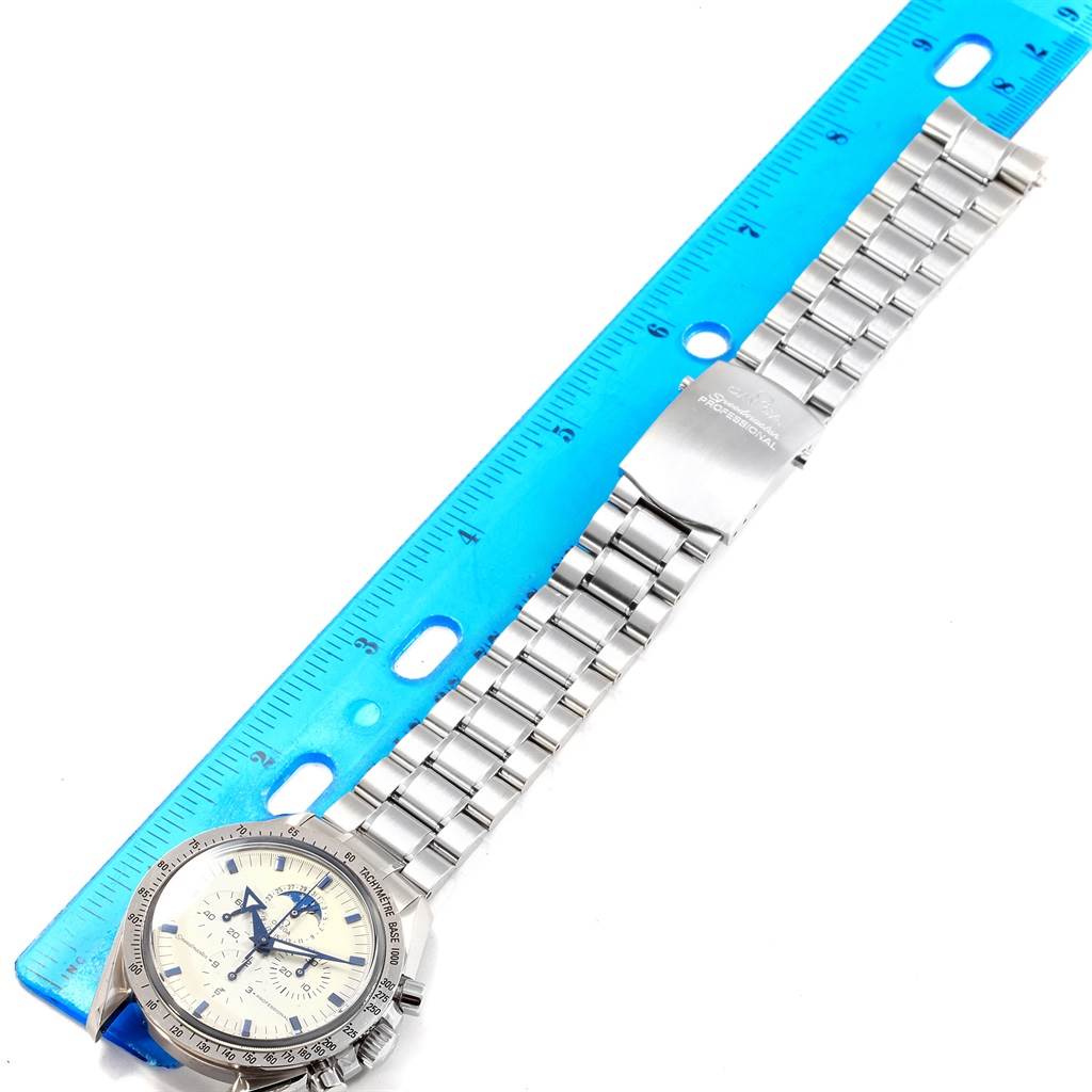 This image shows an Omega Speedmaster 3575.20.00 Men
s Stainless Steel White Dial 3575.20.00 Men
s Stainless Steel White Dial watch with a metal bracelet and clasp laid next to a blue ruler for measurement.