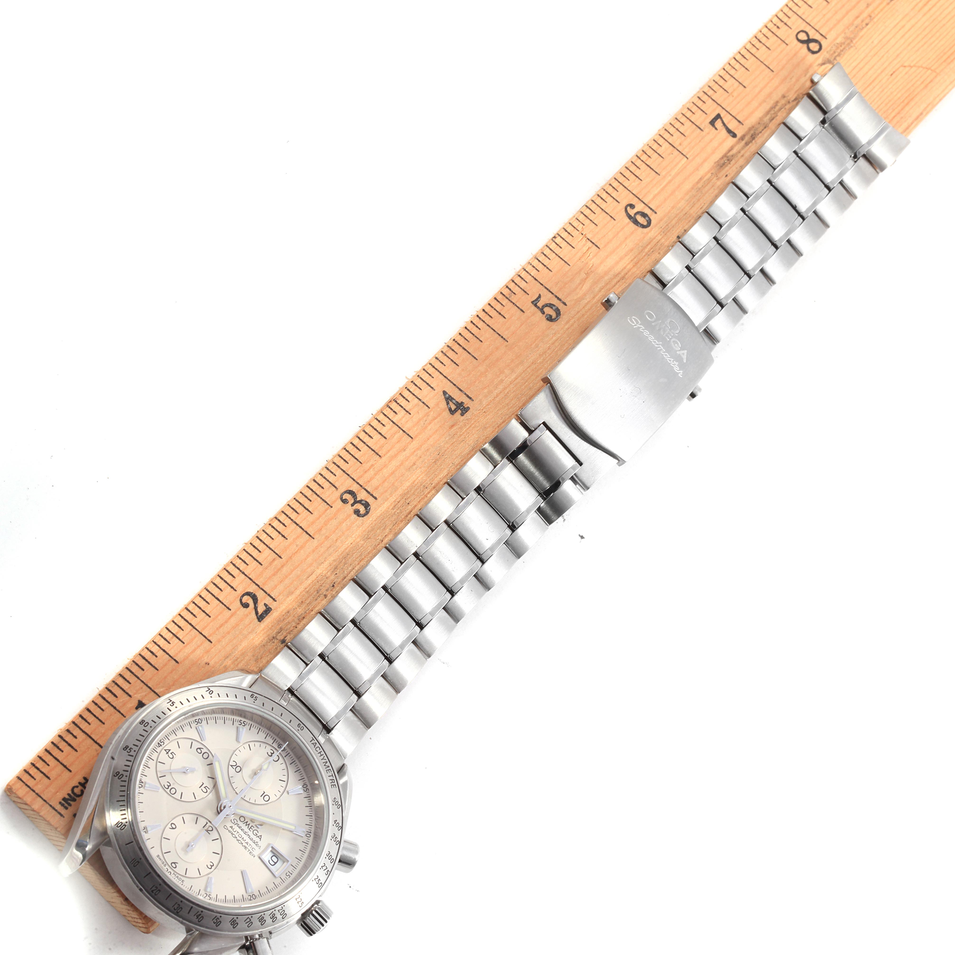 The Omega Speedmaster 3211.30.00 Men
s Stainless Steel Silver Dial 3211.30.00 Men
s Stainless Steel Silver Dial watch is shown at a top-down angle, featuring the face, bezel, and metal bracelet alongside a ruler for scale.