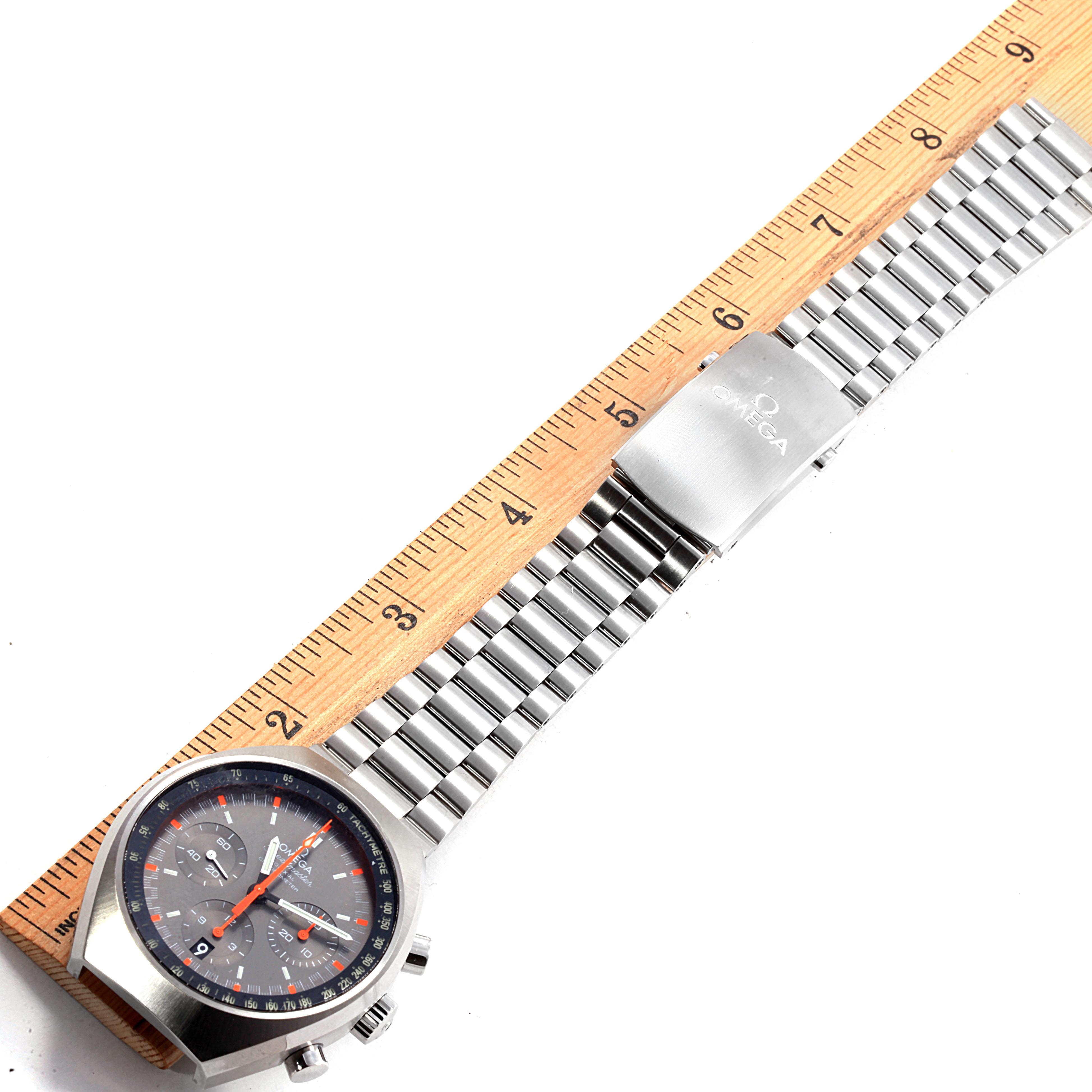 The image shows an Omega Speedmaster 327.10.43.50.06.001 Men
s Stainless Steel Grey Dial 327.10.43.50.06.001 Men
s Stainless Steel Grey Dial watch with a metal bracelet next to a ruler for measurement.