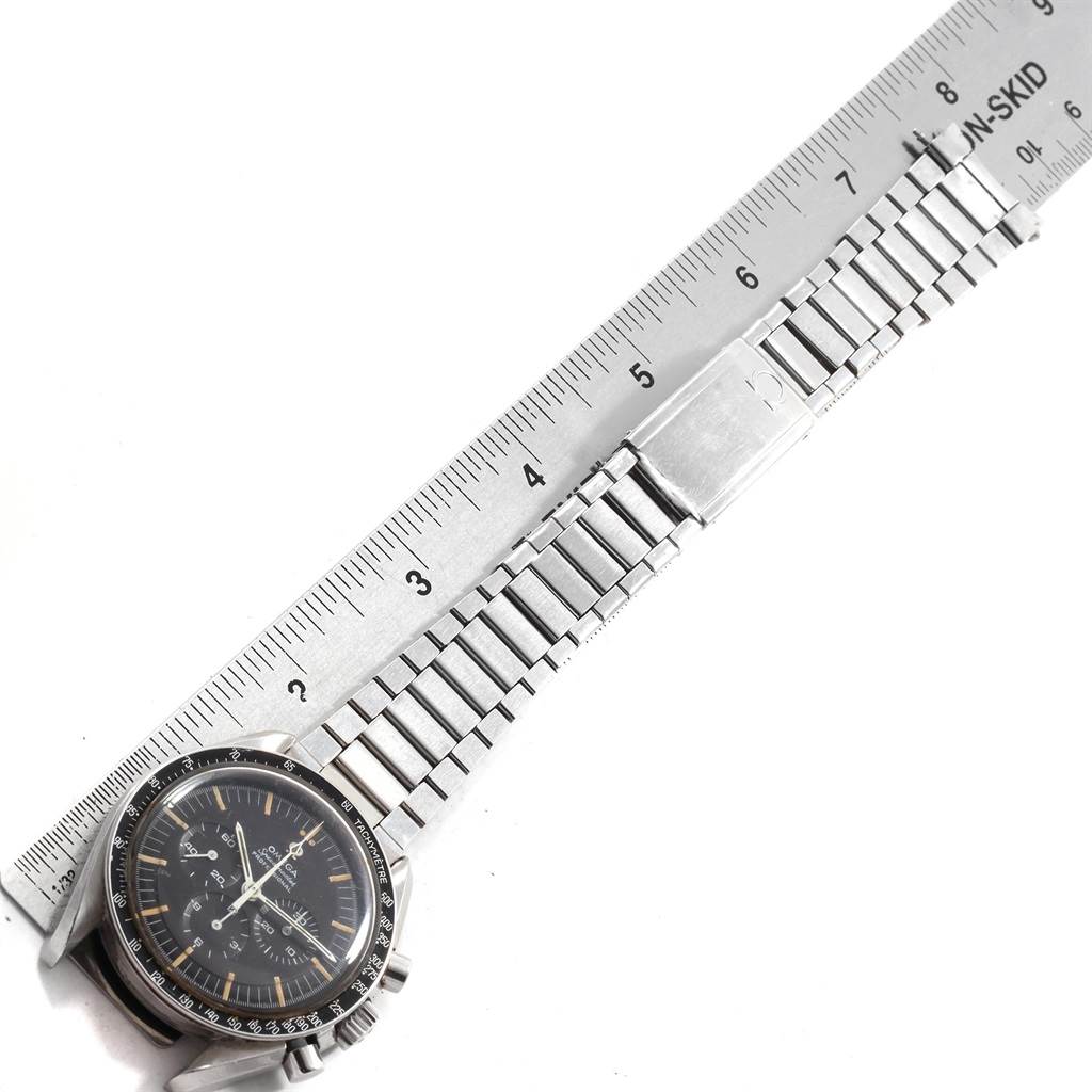 The image shows the Omega Speedmaster 145.012 Men
s Stainless Steel Black Dial 145.012 Men
s Stainless Steel Black Dial watch and its metal bracelet, with a ruler indicating its length.