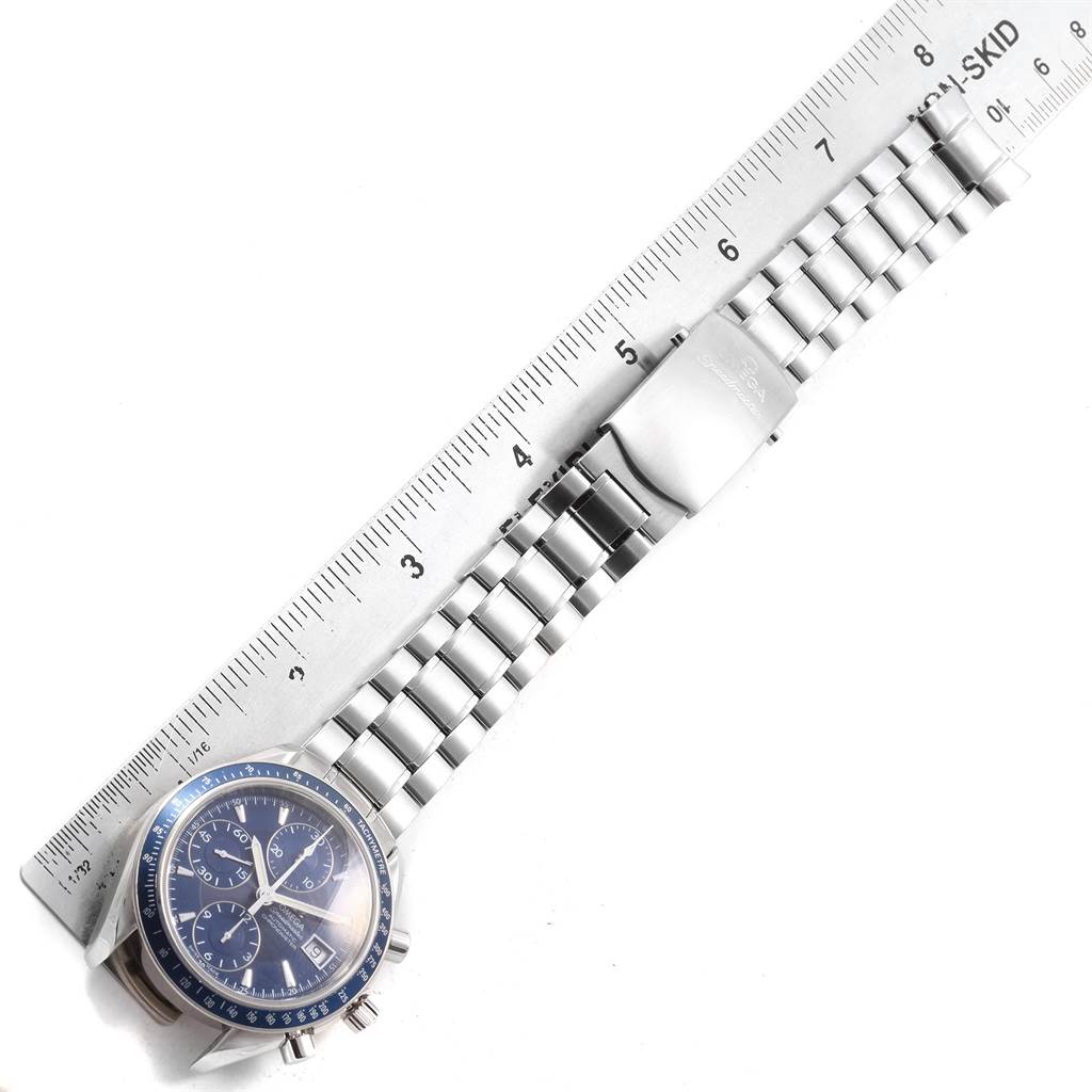 The Omega Speedmaster 3212.80.00 Men
s Stainless Steel Blue Dial 3212.80.00 Men
s Stainless Steel Blue Dial watch is shown from an overhead angle, displaying its face, bracelet, and clasp, alongside a metal ruler.