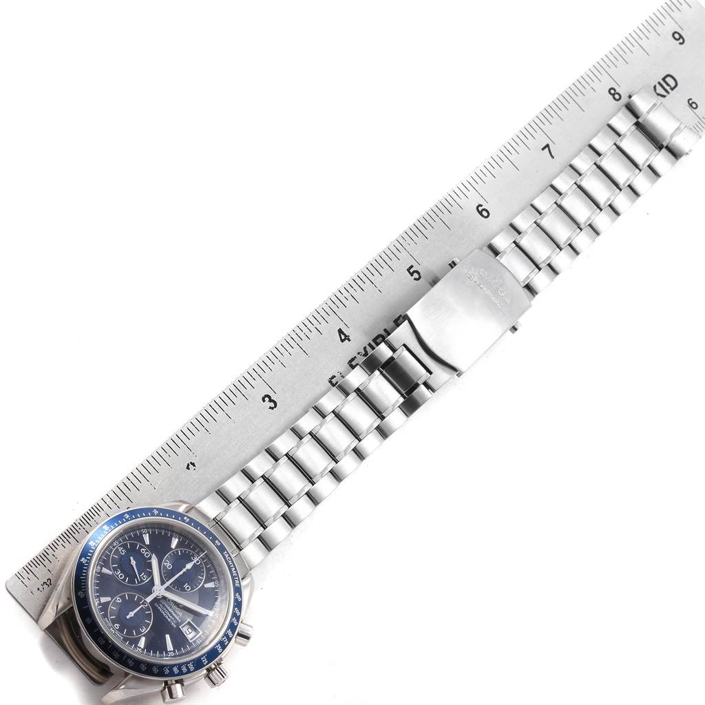 The image shows an Omega Speedmaster 3212.80.00 Men
s Stainless Steel Blue Dial 3212.80.00 Men
s Stainless Steel Blue Dial watch laid flat with a metal ruler, displaying the face, crown, and bracelet.
