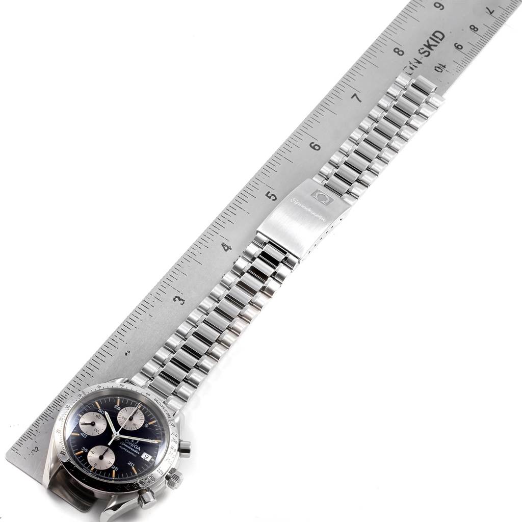 The image shows an Omega Speedmaster 3511.50.00 Men
s Stainless Steel Black Dial 3511.50.00 Men
s Stainless Steel Black Dial watch laid flat with a metal ruler next to it, highlighting the dial, bracelet, and clasp.
