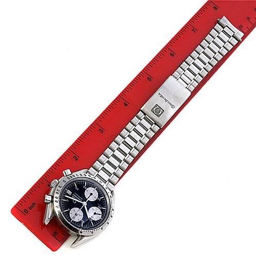 The Omega Speedmaster 3511.   50.   00 Men
s Stainless Steel Black Dial 3511.   50.   00 Men
s Stainless Steel Black Dial watch is shown from a top view displaying its dial, bezel, and metal bracelet placed along a red ruler.