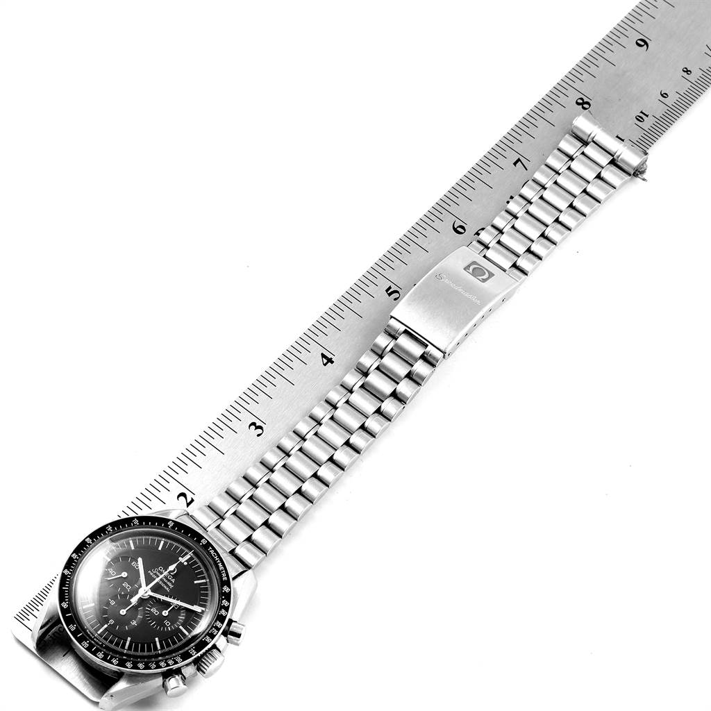 The image shows the Omega Speedmaster 145.022-69 Men
s Stainless Steel Black Dial 145.022-69 Men
s Stainless Steel Black Dial watch laid flat, displaying its face, bezel, and metal bracelet alongside a ruler.