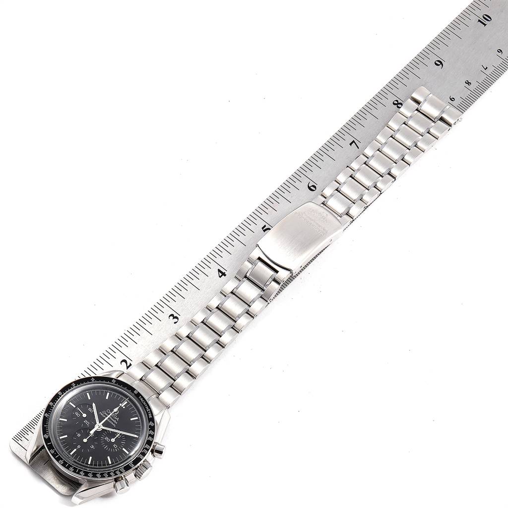 The image shows an Omega Speedmaster 3572.50.00 Men
s Stainless Steel Black Dial 3572.50.00 Men
s Stainless Steel Black Dial watch laid flat next to a ruler, highlighting its watch face and metal bracelet.