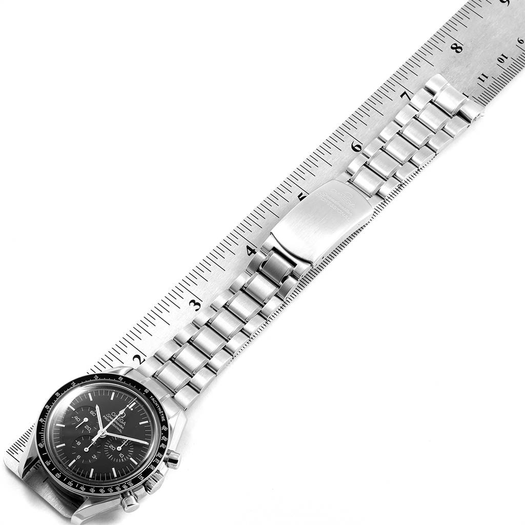 The image shows the Omega Speedmaster 3560.50.00 Men
s Stainless Steel Black Dial 3560.50.00 Men
s Stainless Steel Black Dial watch laid flat against a ruler, showcasing the dial and metal bracelet.