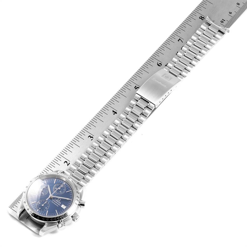 The image shows an Omega Speedmaster 3511.80.00 Men
s Stainless Steel Blue Dial 3511.80.00 Men
s Stainless Steel Blue Dial watch laid flat on its side with its metal bracelet extended, alongside a ruler for scale.