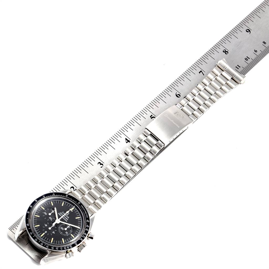 The image shows an Omega Speedmaster Men's Stainless Steel Black Dial Men's Stainless Steel Black Dial watch laid flat alongside a ruler, highlighting the bracelet and clasp.