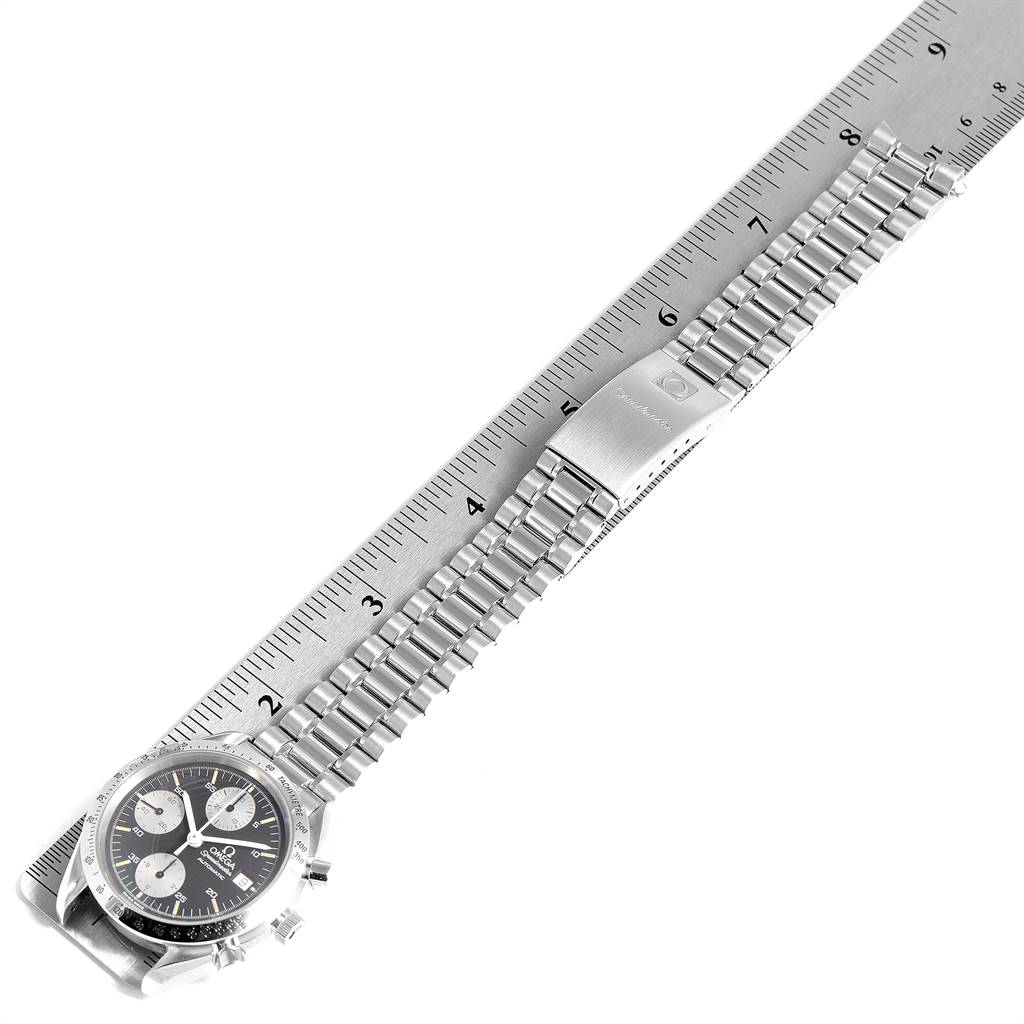 The image shows the Omega Speedmaster 3513.51.00 Men
s Stainless Steel Black Dial 3513.51.00 Men
s Stainless Steel Black Dial watch with a metal bracelet laid on a ruler, displaying the watch face and clasp.