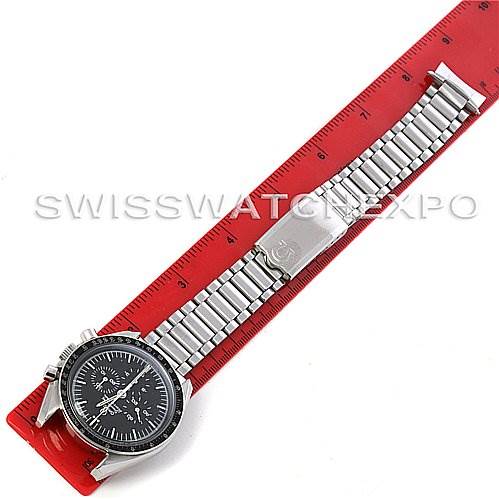 The image shows a top-down view of an Omega Speedmaster Men
s Stainless Steel Black Dial Men
s Stainless Steel Black Dial watch with a stainless steel bracelet placed beside a red ruler.
